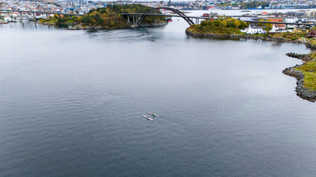 Aerial view of kayaks paddling in a calm bay with a bridge and cityscape in the background.の写真素材