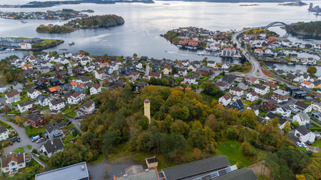 Aerial view of a coastal town with a mix of modern and traditional houses, surrounded by water and small islands. A tall, narrow tower stands in a wooded area in the foreground.の写真素材