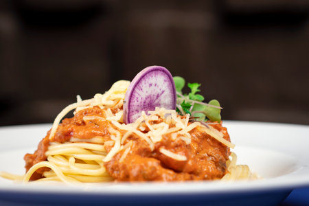 spaghetti bolognese on dish, garnished with some leaves and vegetable, detail shot.の写真素材