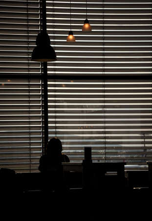 backlit person sitting in an airport cafe in front of a shuttered windowの写真素材