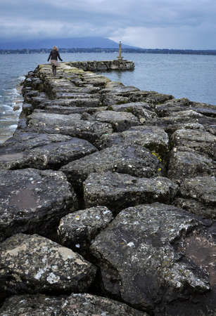 blonde woman walking on a stone pier at lake geneva, switzerland, landscape.