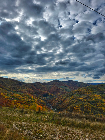 Colorful autumn mountain landscape with green, yellow, orange and red trees on a cloudy day.