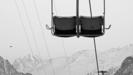 2-seater chairlift with Austrian mountains in the background in black and whiteの写真素材