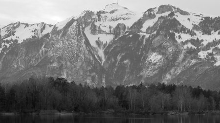 Quarry pond with forest and mountains in background in winter at Paspels Baggerloch in Rankweil, Austria in black and whiteの写真素材