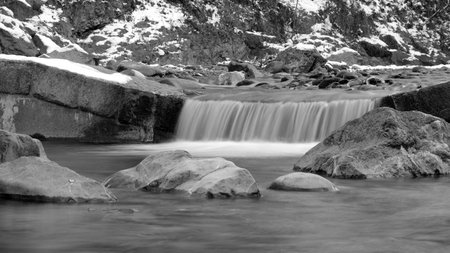 Small waterfall from a stream in winter with big stones in water in black and whiteの写真素材