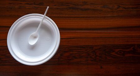 Disposable white plastic plate and spoon in a wooden tableの写真素材