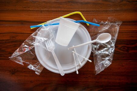 Some pieces of a disposable white plastic crockery in a wooden table.