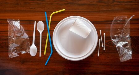 Some pieces of a disposable white plastic crockery in a wooden table.