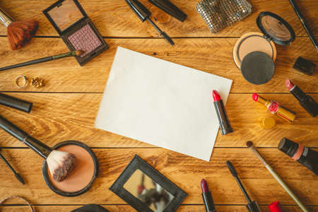 A blank sheet paper to write a note, on a wooden table with makeup products around.の写真素材