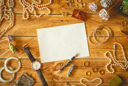 A blank sheet paper to write a letter on a wooden table with some memories and jewelry