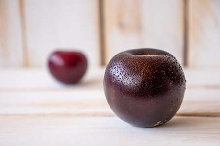 Some dark ripe plums on a white wooden wall and table.