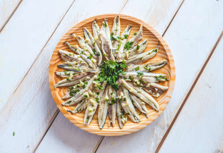 Pickled anchovies with garlic and parsley in a round wooden plate on a white wooden table. Typical Spanish snack.の写真素材