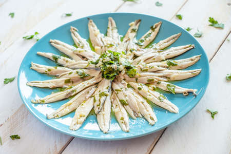 Pickled anchovies with garlic and parsley marinated in vinegar in a round wooden plate on a white wooden table. Typical Spanish snack.の写真素材