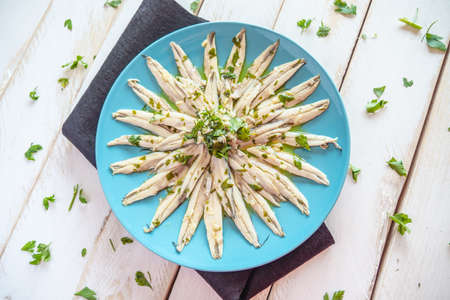 Pickled anchovies with garlic and parsley marinated in vinegar in a round wooden plate on a white wooden table. Typical Spanish snack.の写真素材