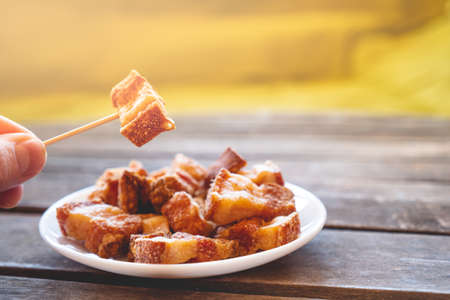Hand holding a piece of fried pork rinds called "Torreznos" with a toothpick on a dark wooden table. Typicall spanish snacks to eat in a bar. Photo with selective focus.の写真素材