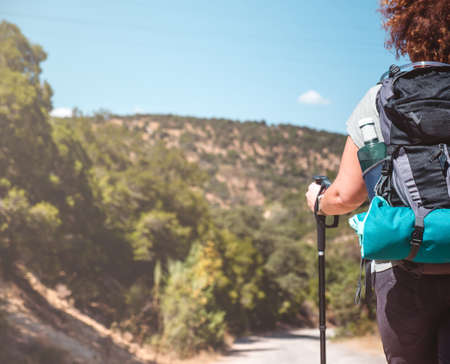 Woman with hiking equipment walking in green mountain landscape on a sunny day.の写真素材