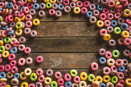 Colorful round fruit cereals scattered on brown wooden table with space in the middle.の写真素材