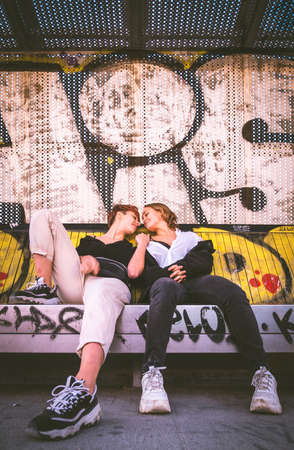 Two girls sitting on a bench against a wall full of graffiti on the street.の写真素材