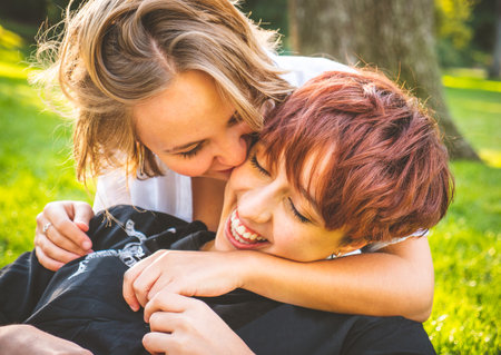 Girls couple in love kissing sitting on the grass in a park on a sunny day.の写真素材