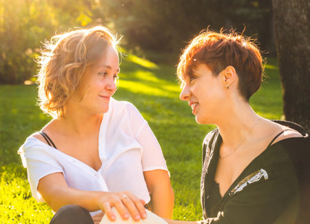 Girls couple in love sitting on the grass in a park on a sunny day.の写真素材