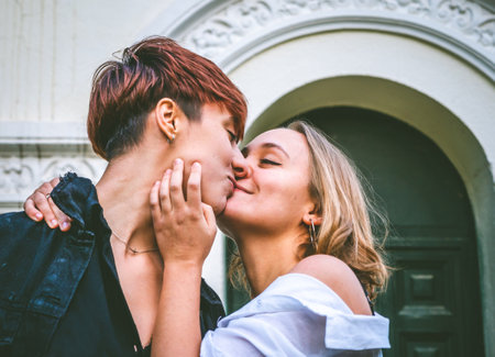Girls couple standing kissing in a dark green door on the street.の写真素材