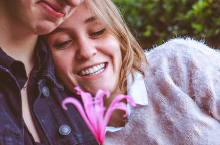 Girls couple in love playing wtih a pink flower sitting in a park. Photo with selective focus.の写真素材