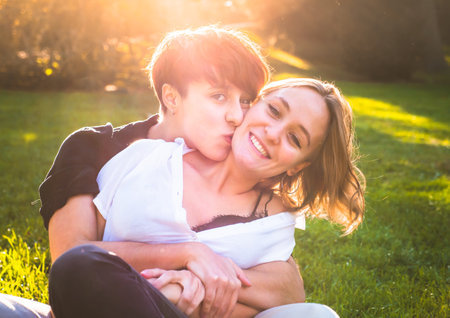 Girls couple in love kissing sitting on the grass in a park on a sunny day.の写真素材