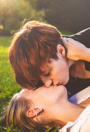 Girls couple in love kissing lying on the grass in a park on a sunny day.の写真素材