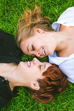 Girls couple in love lying on the grass in a park on a sunny day.の写真素材