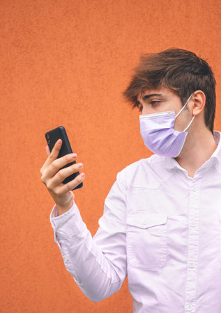 Guy with purple face mask looking at his smartphone on an orange background.の写真素材