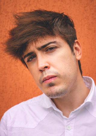 Serious guy in white shirt smiling on an orange wall.の写真素材