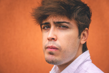 Serious guy in white shirt smiling on an orange wall.の写真素材