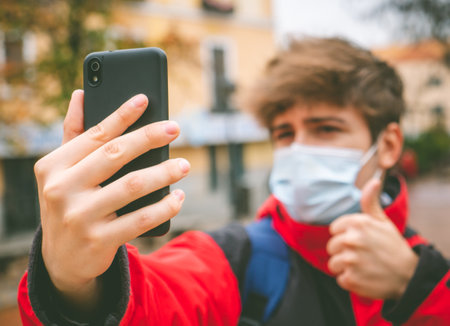 Guy with face mask and backpack taking a selfie in the street on a winter day.の写真素材