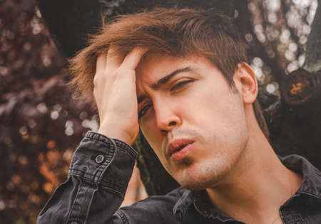 Guy touching his hair staring in camera in a park.の写真素材