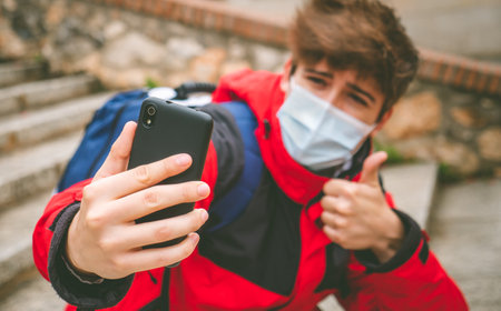 Guy with face mask and backpack taking a selfie in street stairs on a winter day.の写真素材