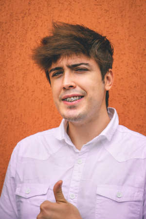 Guy in white shirt smiling and rising thumb on an orange wall.の写真素材