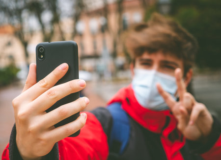 Guy with face mask and backpack taking a selfie in the street on a winter day.の写真素材
