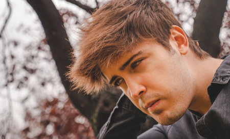 Guy with hand on nape looking aside in a park on an autumn day.の写真素材