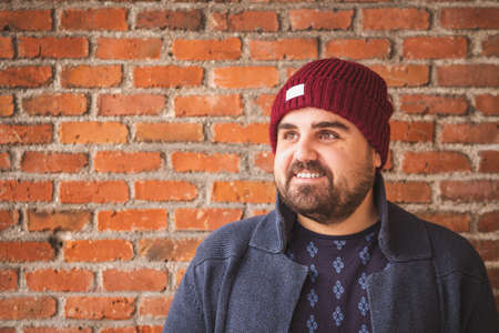 oarded guy in a woolen hat and sweater smiling on a brick wall.の写真素材