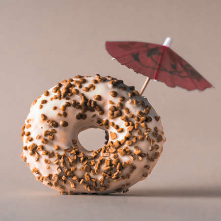 White chocolate donut with almonds topping and a decoration umbrella on gray background.の写真素材