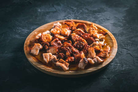 "Galician octopus". Plate of chopped octopus with oil and paprika in a round wooden plate on a dark table. Typical food of Galicia, Spain.の写真素材