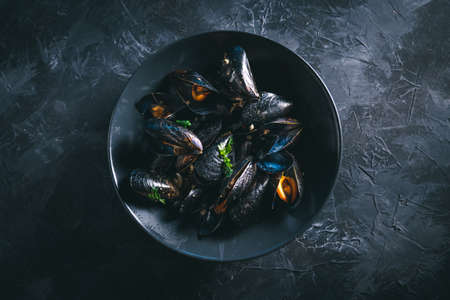 Steamed mussels in a black bowl on a dark table. Easy and cheap seafood recipe. Photo with selective focus.の写真素材