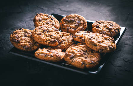 Homemade chocolate chip cookies on a black square plate on a dark table. Ready to eat.の写真素材