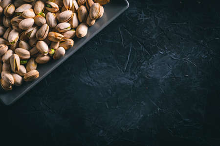 Pistachios in a gray rectangular plate on a dark table. Ready to eat nuts. Energy food.の写真素材