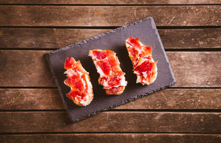 Iberian ham toasts on a slate plate on a brown wooden. Spanish typical food. Pork meat.の写真素材
