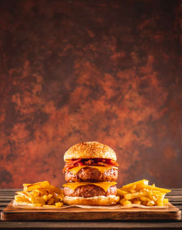 Double beef and bacon burger with cheddar cheese and chips on a wooden board on a table, ready to eat. Size XL.の写真素材