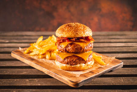 Double beef and bacon burger with cheddar cheese and chips on a black plate on a dark table, ready to eat. Photo with copy space.の写真素材