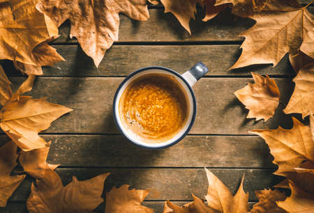 Hot coffee cup on an aged wooden table with autumn leaves around it. Homey feeling and relax.の写真素材