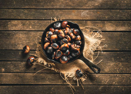 Roasted chestnuts in a small iron pan on an aged brown wooden table. Ready to eat. Traditional autumn food.の写真素材