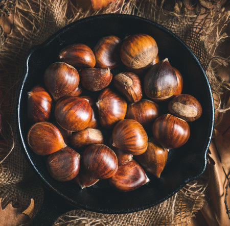 Raw chestnuts in a small iron pan on a table with autumn leaves and pine cones. Ready to roast and eat. Traditional autumn food.の写真素材